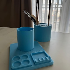 Op de afbeelding: Een lichtblauwe bureau-organizer set bestaande uit een cilindrische beker met meerdere gaten voor penselen, een aparte beker en een rechthoekige basis met gevormde uitsparingen en de tekst "3D PRO DESIGN" in reliëf op het oppervlak.