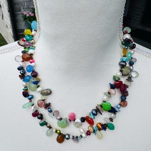 May include: A multi-strand necklace featuring an assortment of colorful gemstones and pearls in various shapes and sizes. The necklace includes beads in shades of red, blue, green, yellow, pink, and white, interspersed with small dark metal spacers.