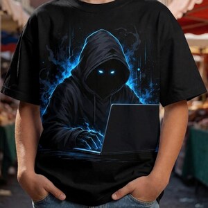 Może przedstawiać: Czarny t-shirt z grafiką przedstawiającą postać w kapturze ze świecącymi na niebiesko oczami, piszącą na laptopie. Postać jest otoczona niebieskimi efektami energii cyfrowej, a wzór znajduje się na środku przodu odzieży.