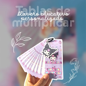 Puede incluir: Un llavero educativo de tablas de multiplicar en color morado claro con un dije de personaje de dibujos animados en blanco y negro. Las tarjetas están unidas por una argolla negra y muestran el texto KUROMI FYTH WORLD y TABLAS DE MULTIPLICAR.