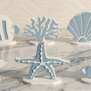 May include: A set of six freestanding wooden figures featuring nautical shapes including a fish, coral, a scallop shell, a sea turtle, a starfish, and a conch shell. Each piece is painted in a matte white and dusty blue color scheme.