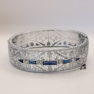 This listing is for an elegant silver tone filigree bracelet. It features blue faceted stones and rhinestones. A beautiful vintage piece Art Deco inspired.