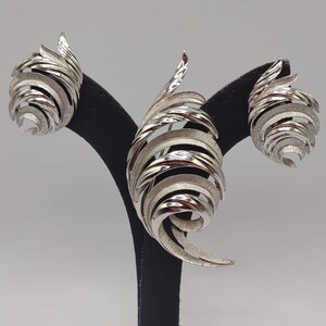 May include: A set of three silver earrings with a spiral design. The earrings are displayed on a black stand.