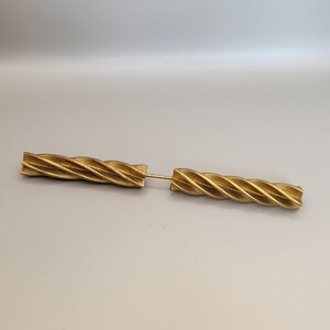 May include: Two gold-colored metal pieces with a twisted design. The pieces are joined together by a small metal pin.