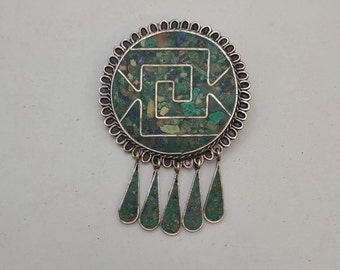 May include: A silver pendant with a green and blue geometric design and a fringe of teardrop-shaped charms.