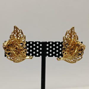 May include: A pair of gold-tone leaf-shaped earrings with a delicate filigree design.