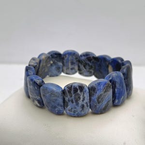 May include: A blue gemstone bracelet made of smooth, oval-shaped beads. The beads have a mottled pattern of dark blue and white.