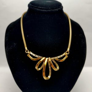 May include: A gold-tone necklace with a bow-shaped pendant adorned with clear rhinestones. The necklace has a delicate chain.