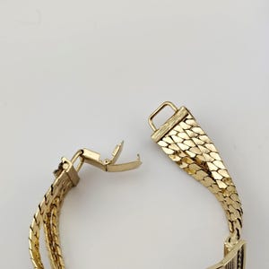 May include: Gold bracelet with a distinctive, textured pattern. The bracelet is made up of interconnected, scale-like segments. The clasp is open, showing the detailed construction. The overall style is vintage and elegant.