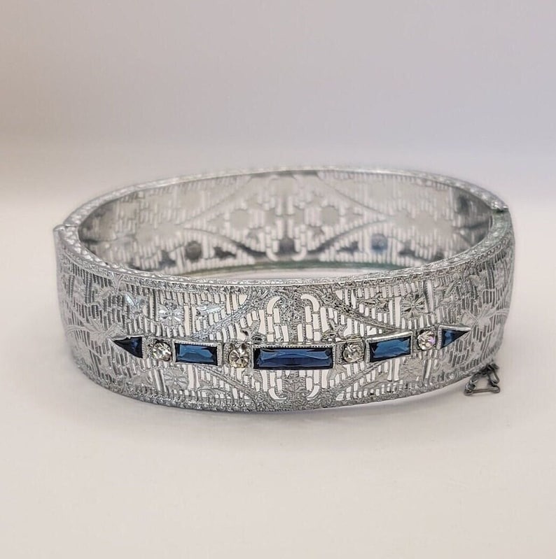 This listing is for an elegant silver tone filigree bracelet. It features blue faceted stones and rhinestones. A beautiful vintage piece Art Deco inspired.