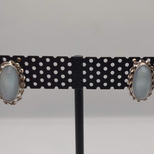 May include: A pair of silver clip-on earrings with oval-shaped white stones set in a decorative silver frame.