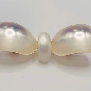 May include: A white pearl bow brooch with a round pearl in the centre.