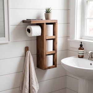 May include: A dark brown wooden wall-mounted bathroom organizer featuring a top shelf, a horizontal toilet paper roll holder, and three vertical storage cubbies for toilet paper rolls. A small potted succulent sits on the top shelf.