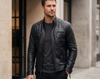 Può includere: Una giacca in pelle nera con colletto alla coreana, chiusura frontale con zip e dettagli trapuntati sulle spalle. La giacca presenta due tasche sul petto con zip e maniche lunghe con polsini con zip, indossata sopra una t-shirt nera.