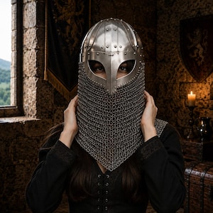 May include: A silver-coloured metal helmet featuring a riveted dome, a central nasal guard, and an integrated chainmail aventail that covers the lower face and neck. The helmet is constructed from polished steel plates with visible rivets.