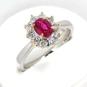 May include: A ring featuring a central oval-cut vibrant red gemstone surrounded by a halo of twelve round brilliant-cut white diamonds. The setting is crafted from a combination of yellow gold prongs and a polished silver-toned metal band.