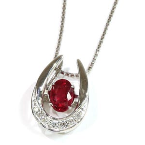 May include: A silver-toned necklace featuring a horseshoe-shaped pendant. The pendant is set with a central oval-cut deep red gemstone and accented with a row of small, clear round stones along the bottom curve, suspended on a box chain.
