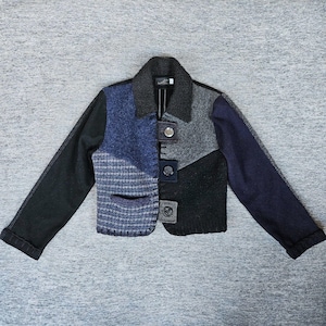 May include: A cropped jacket featuring a patchwork design of various wool-like textures in shades of black, charcoal gray, and navy blue. The garment includes a dark collar, long sleeves, and a front closure with three distinct button tabs.