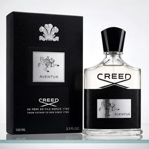 May include: A 100 ml, 3.3 fl. oz. bottle of Creed Aventus fragrance with a black cap and a black and silver label featuring a horseman graphic. Beside it stands a matching black rectangular box with the same silver emblem and text.