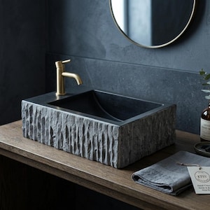 Peut inclure: Un lavabo rectangulaire en pierre avec une texture extérieure brute et ciselée et un bassin intérieur lisse. Il est équipé d'un robinet en métal doré sur le côté. Un linge en lin gris avec une étiquette indiquant Etsy Hand-Chiseled Stone & Resin.