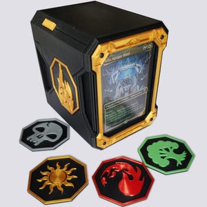 May include: A black and gold rectangular trading card storage box with a clear front display window holding a Kilo, Apogee Mind card. Four hexagonal tokens are placed in front, featuring a grey skull, a gold sun, a red flame, and a green tree.