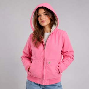 May include: A bright pink zip-up hooded jacket featuring a white sherpa fleece lining, long sleeves with ribbed cuffs, and a front kangaroo pocket. A small rectangular Carhartt brand label is stitched onto the lower right side of the front pocket.