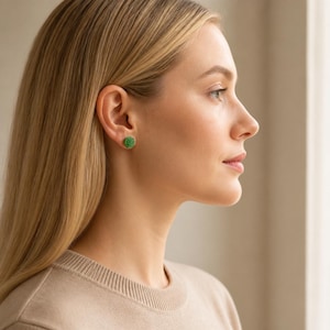 Peut inclure: Une petite boucle d'oreille à clou ronde de couleur verte avec un motif texturé inspiré d'une fleur. La boucle d'oreille est portée au lobe, présentant une couleur verte vive et un motif détaillé de pétales superposés en forme circulaire.