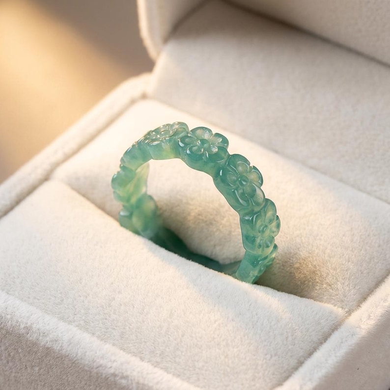 May include: A translucent light green ring carved from a single piece of stone, featuring a continuous band of repeating five-petaled flower motifs. The ring has a smooth, polished finish and a consistent pale mint-green color throughout the band.