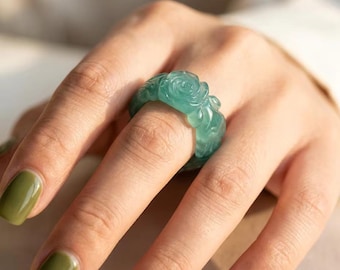 May include: A translucent teal green ring featuring a carved floral rose pattern that wraps around the entire band. The ring has a smooth, polished finish and a rounded profile, showcasing intricate petal details carved directly into the material.