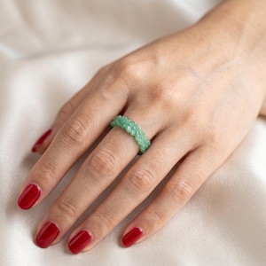 May include: A light green ring carved from a single piece of stone, featuring a continuous band of small, detailed floral motifs encircling the entire circumference of the ring. The surface of the band has a smooth, polished, and translucent finish.