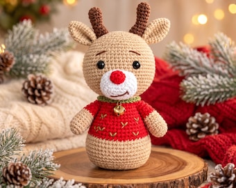 May include: A crocheted reindeer amigurumi toy with a tan body, dark brown antlers, and a bright red nose. The reindeer wears a red sweater with small green leaf embroidery and a gold jingle bell attached to a green collar around its neck.