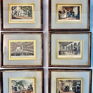 May include: A set of six framed historical prints featuring detailed color illustrations of 18th-century social scenes, each enclosed in a dark wood frame with a light gray mat and a thin gold border, displaying various indoor and outdoor settings.