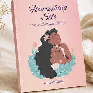 May include: A softcover book titled Flourishing Solo: A 31-Day Guide to Embracing Independence and Navigating Through Life Freely by Ashley Kidd. The cover features a pink background with an illustration of a person with long dark hair.