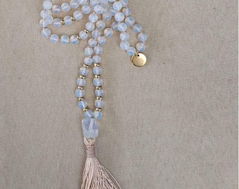 May include: A long necklace featuring translucent, pale blue spherical beads interspersed with small metallic gold spacers. The necklace includes a larger, irregular-shaped pale blue bead above a long, light beige thread tassel.