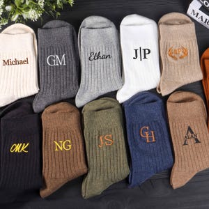 Puede incluir: Una colección de diez calcetines acanalados en varios colores, incluyendo crema, carbón, gris claro, blanco, bronceado, negro, marrón, verde oliva y azul marino. Cada calcetín presenta texto o iniciales bordadas únicas como Michael, GM, Ethan, J|P, AP con astas, CMK, NG, JS, GH y ALAN.