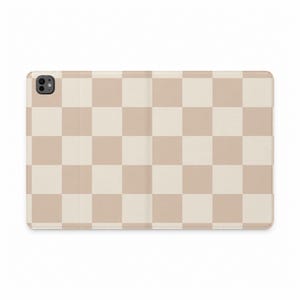 Peut inclure: Une housse de tablette rectangulaire présentant un motif en damier répétitif alternant des nuances de beige clair et de crème. L'étui comprend une découpe circulaire dans le coin supérieur gauche pour l'objectif de l'appareil photo.