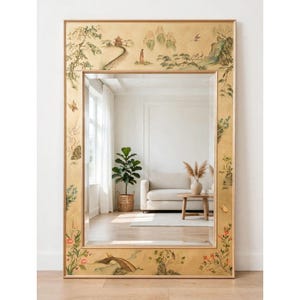 May include: A large rectangular wall mirror featuring a wide gold-toned frame decorated with hand-painted chinoiserie motifs, including a pagoda, a winding path, lush trees, delicate floral vines, and small birds across the top and bottom borders.