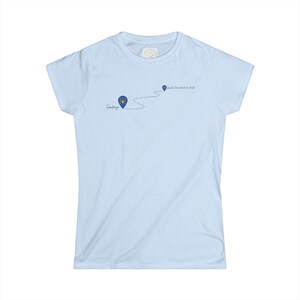 以下が含まれることがあります： ライトブルーの半袖Tシャツ。2つのダークブルーの地図ピンを繋ぐ点線のルートが描かれています。ピンにはそれぞれ「Santiago」と「Saint Jean Pied de Port」という文字があり、最初のピンの中には小さな黄色いエンブレムがデザインされています。