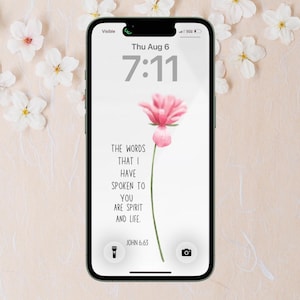 Puede incluir: Un teléfono inteligente que muestra un fondo de pantalla digital con una ilustración de una flor rosa y el texto: THE WORDS THAT I HAVE SPOKEN TO YOU ARE SPIRIT AND LIFE. JOHN 6:63. La pantalla muestra la hora 7:11 y la fecha Thu Aug 6.
