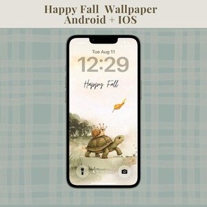 May include: A smartphone displaying a digital wallpaper with the text Happy Fall Wallpaper Android + IOS at the top. The screen shows a watercolor illustration of a snail riding on a turtle with a falling orange leaf and the text Happy Fall.