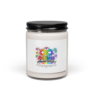 May include: A white candle in a glass jar with a black lid, featuring a label with a rainbow-colored infinity symbol and the text Autism Awareness, along with phrases like Different Brains, Accept, Include, Support, Empower, and A Kinder, More Inclusive Tomorrow.