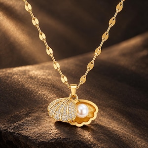 May include: A gold-toned necklace featuring a pendant shaped like an open seashell. The exterior of the shell is encrusted with small clear stones, while the interior holds a single white pearl. The chain consists of elongated, flat gold links.