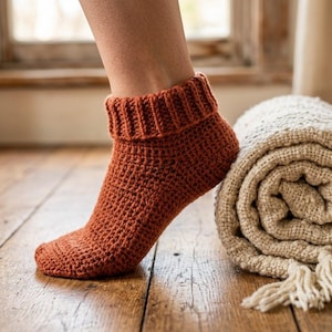 May include: A rust-coloured ankle sock featuring a thick, ribbed cuff and a textured, crocheted knit pattern. The sock is constructed with a dense stitch design that covers the foot and ankle, providing a uniform appearance in a solid earth tone.