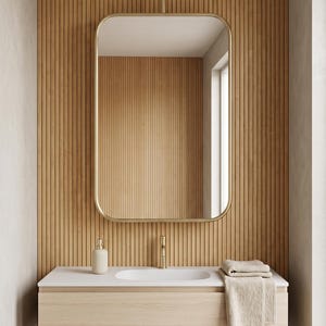 Könnte beinhalten: Ein wandmontierter Waschtisch mit hellem Holzfinish, weißer Arbeitsplatte und integriertem Waschbecken. Ein goldfarbener Wasserhahn und ein passender rechteckiger Spiegel mit abgerundeten Ecken hängen von der Decke. Ein beiges Handtuch liegt auf.