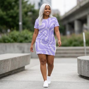 Puede incluir: Un vestido de manga corta por encima de la rodilla con un patrón repetitivo de ondas y remolinos en color lavanda y morado claro. La prenda tiene un cuello redondo, una silueta ajustada y se combina con zapatillas blancas sencillas.