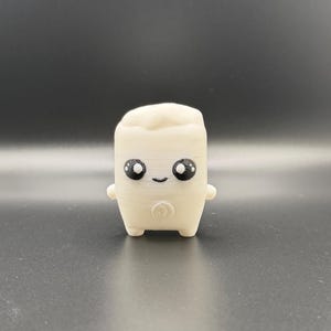 May include: A small, off-white, 3D-printed figurine shaped like a marshmallow. It features a smooth, cylindrical body with two tiny arms and legs, and a face with large, black, glossy eyes and a small, simple, curved black mouth.