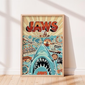 May include: A framed poster featuring a large shark head with open jaws at the bottom. The design includes the text JAWS, a person swimming, a boat, a lighthouse, and various vintage-style stickers with phrases like BEACH CLOSED and BIGGER BOAT.