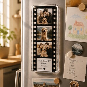 May include: A rectangular magnetic photo frame designed like a film strip, featuring three vertical photo slots containing images of a couple with a golden retriever. The bottom section displays the text OUR FAMILY STORY EST. 2026 with a small heart icon.