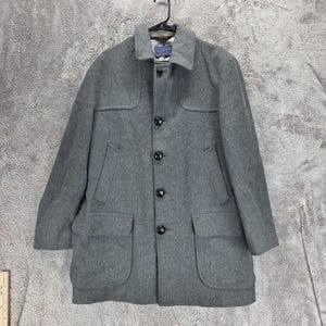 May include: A grey wool coat featuring a collared neckline, a front button closure with five black buttons, two slanted chest pockets, and two large flap pockets at the waist. The interior label displays the Pendleton brand name in blue text.