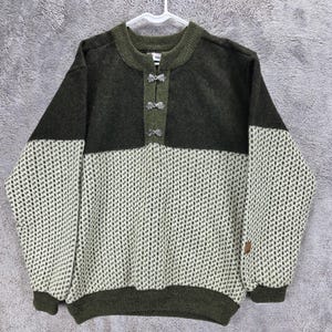 May include: A long-sleeve pullover sweater featuring a dark olive green upper section and a cream-colored lower section with a repeating dark green geometric pattern. The sweater has a round neckline with three silver-toned metal clasps at the front.